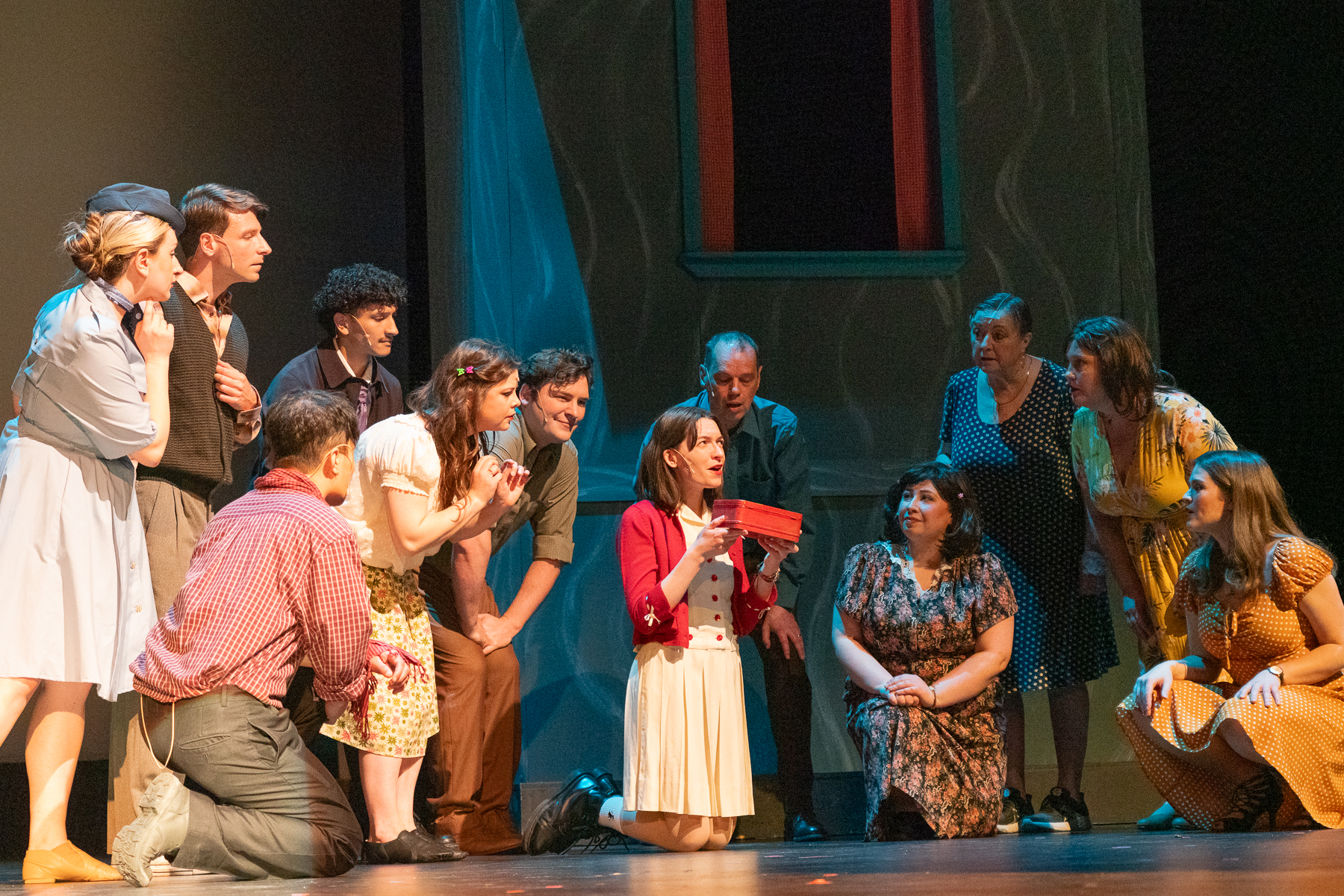 Actor on her knees holding an old red metal box, surrounded by other actors.